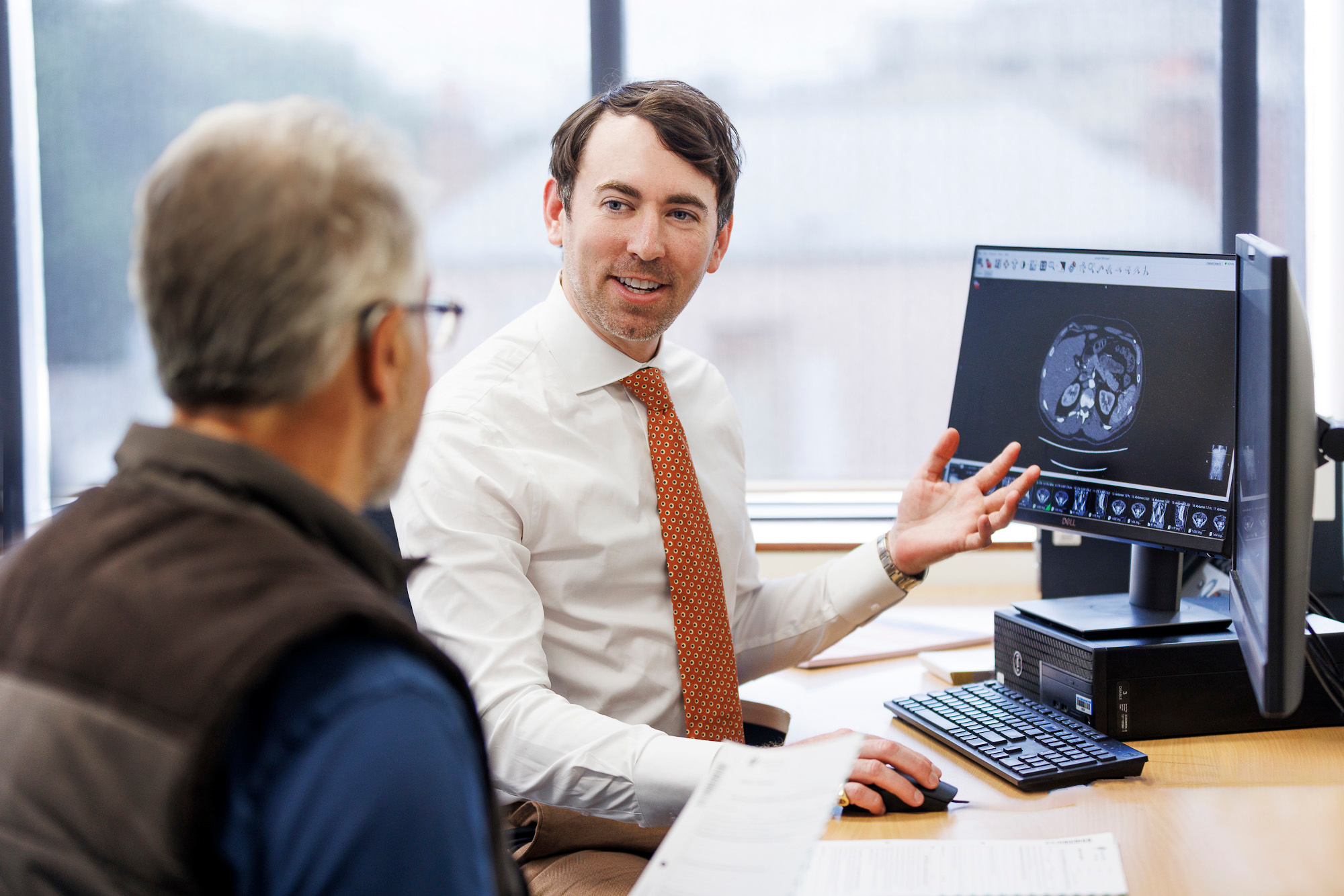 Dr Steel Scott sitting at a computer with a patient, showing them some radiology images Dr Steel Scott sitting at a computer with a patient, showing them some radiology images